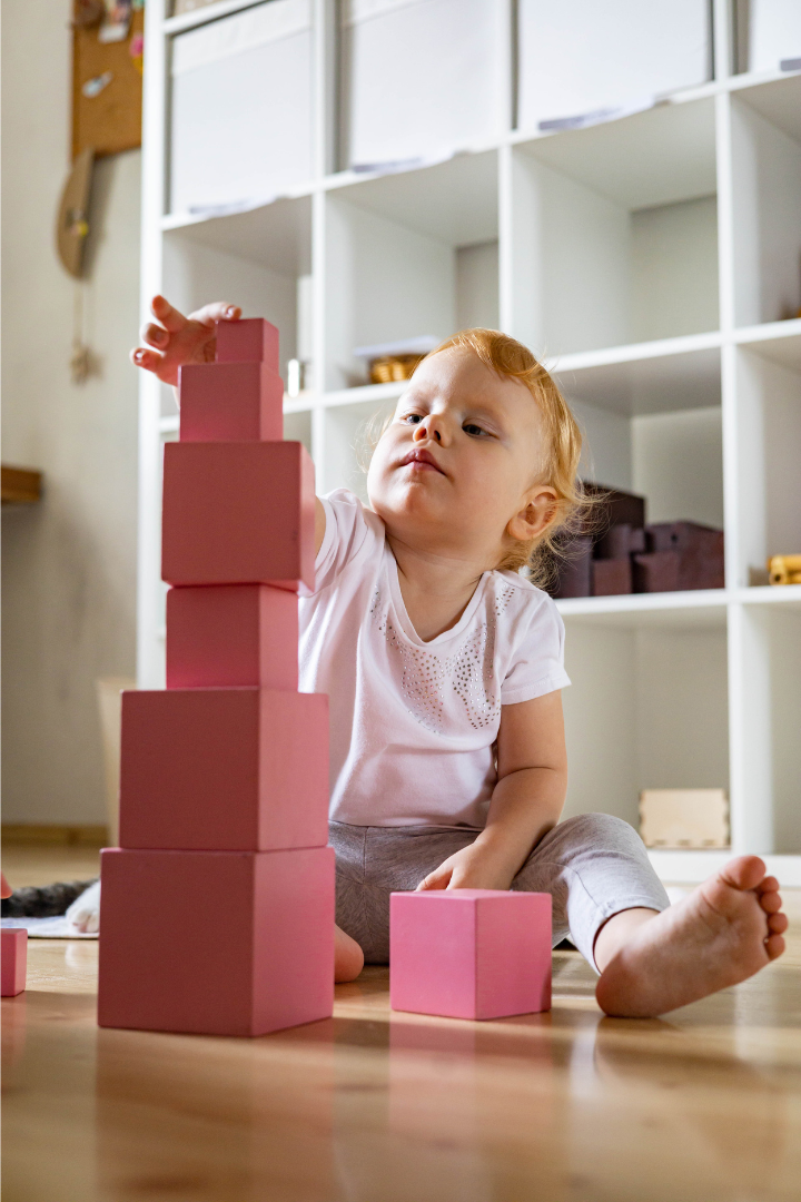 Enfant de 1 ans jouant avec la tour rose Montessori et empilant des cubes en bois.